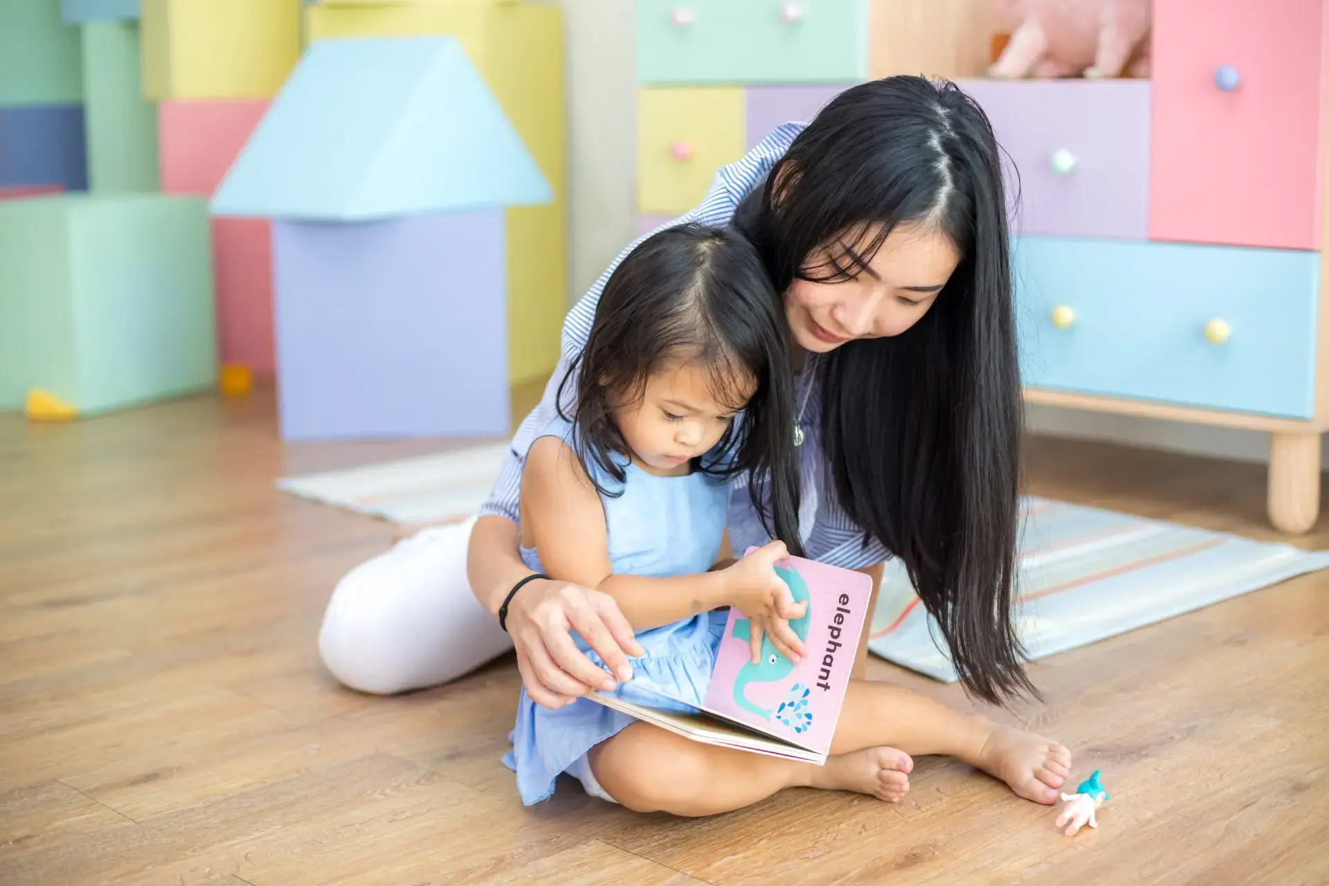 Asyanong nanay at batang anak na babae na nagbabasa ng libro.