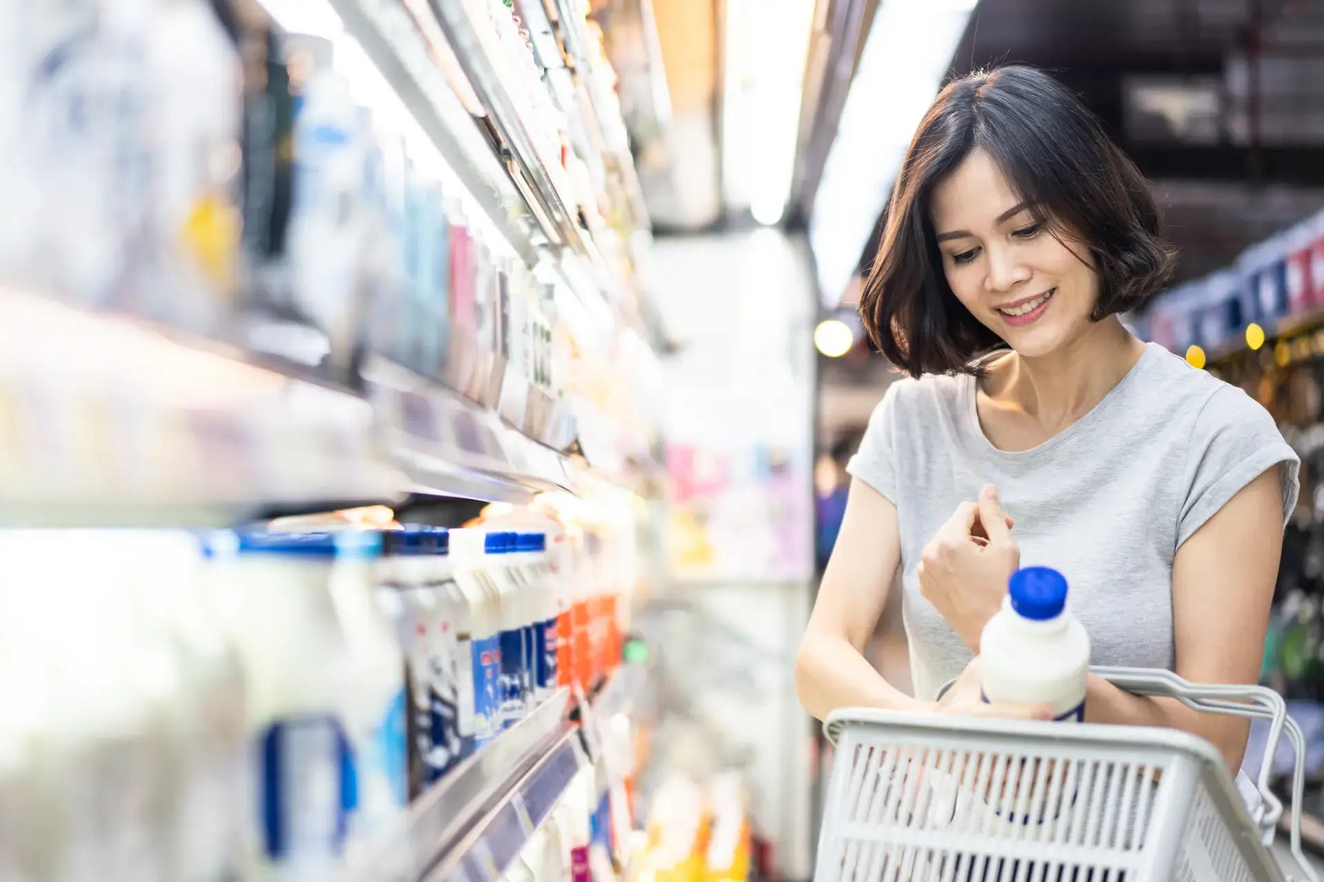 Asyanong babae na nasa grocery linalagay ang isang bote ng gatas sa basket.