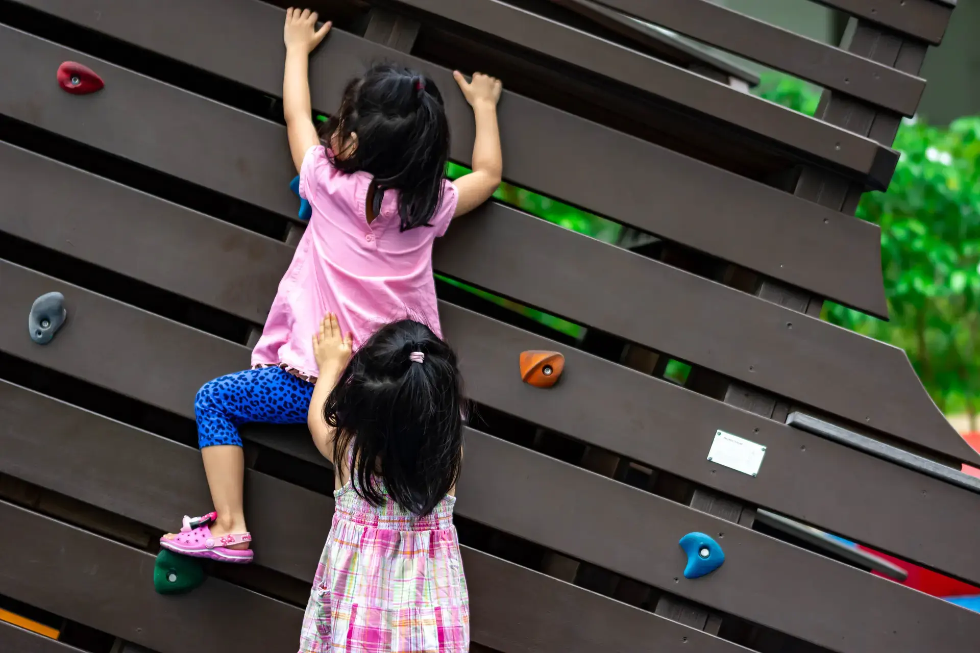 Dalawang Asyanong mga batang babae na nagtutulungan sa pagakyat sa isang parte ng playground.