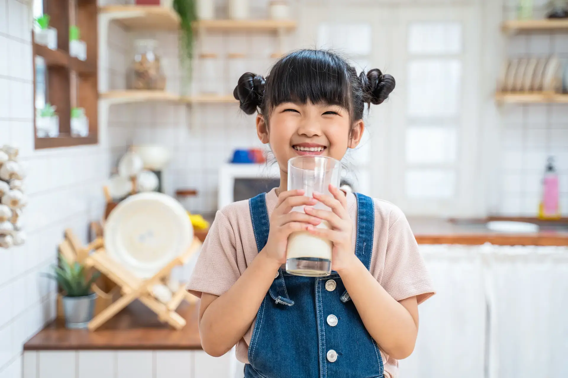 Masayang batang Asyano na may hawak na isang baso ng gatas.