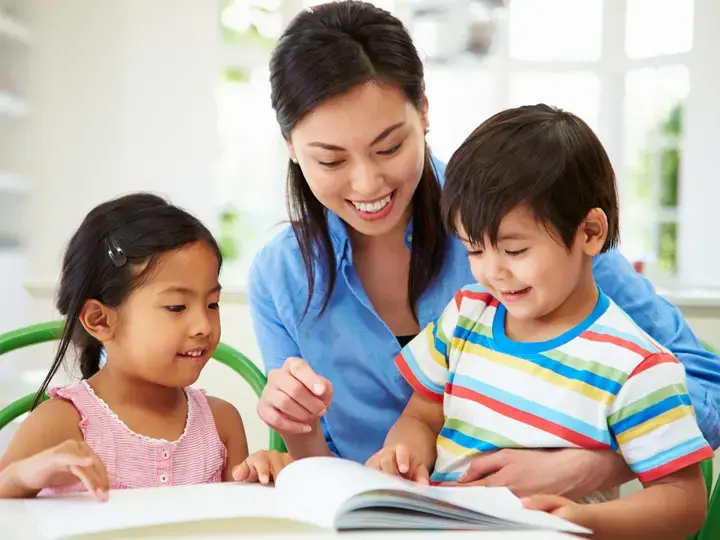 Asyanong batang babae at lalaki na nagbabasa ng libro kasama ang kanilang nanay.